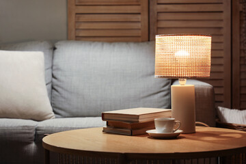 Glowing lamp with books and cup of coffee on table in living room at night