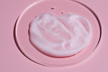 pink cosmetic face cream or body lotion moisturizer strokes on pastel pink background in petri dish. Hygiene, skincare product with creamy texture. Beauty face creme smear swatch on color background