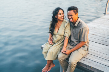 A beautiful moment of joy as a couple sits on a wooden pier, sharing laughter and warmth. The woman...