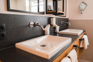 Luxurious bathroom featuring a double sink vanity with black countertop, wooden cabinetry, black framed mirrors, and organized toiletries in Ischgl, Austria.
