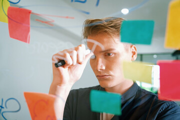 Professional caucasian businessman brainstorming marketing idea by using mind map and sticky notes on glass board at modern meeting room. Creative business and planing concept. Immaculate.