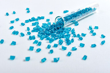 Clear blue masterbatch granules spilled from glass tube and isolated on white background. Color...