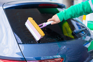 Cleaning the rear window of a car at a service station during the day