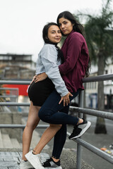two latina lesbian women posing hugging on the street while looking straight ahead
