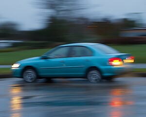 A fast moving teal car seen in a blurred motion photograph
