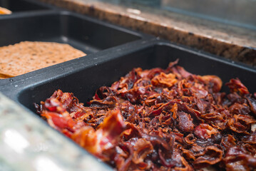 Close up of a buffet station featuring crispy bacon and flatbread on a granite countertop, reflecting an upscale dining environment in Ischgl, Austria.