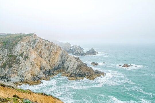 Dramatic coastal cliffs meet turbulent ocean under a misty sky