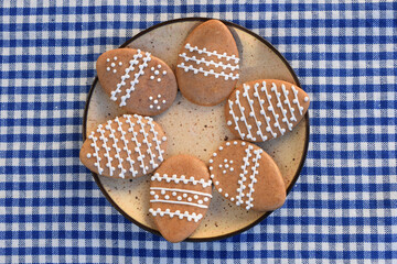 Plate with Easter gingerbread cookies in a shape of egg, checkered background