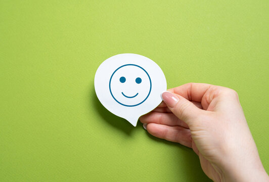 Smiling face on sticker in woman's hand. The concept of good mood and mental health. Optimism, happiness, maintain a balanced mindset. Stress relief, mindfulness practices.