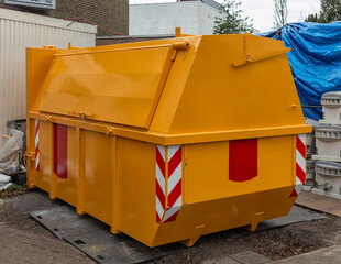 yellow metal industrial waste container with closed steel hatch stands outside on a site