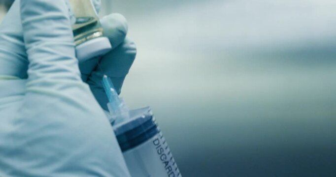 Primer plano de investigador en laboratorio. Investigador usa guantes y sostiene una jeringa en preparaci&oacute;n para paciente.