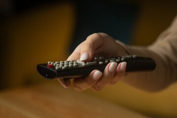 A close-up view shows a hand grasping a remote control, poised to switch to a favorite show or navigate through channels in a cozy living room setting. 
