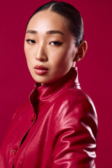 Fashion asian brunette in red leather jacket posing against pink background