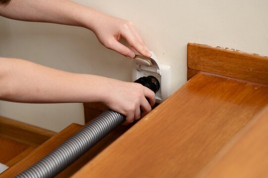 Teenager doing while with household chores in a cozy living space. Closeup of plugging central vacuum cleaner hose in to wall inlet socket.