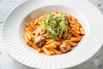 Delicious pasta with meatballs served in a creamy tomato sauce, garnished with fresh greens. A perfect dish for Italian cuisine lovers.
