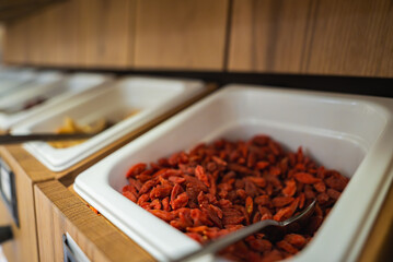 A buffet setup with white trays on a wooden counter, featuring dried goji berries in the foreground with a metal spoon, in a luxury hotel in Ischgl, Austria.