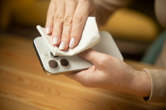 Hands are cleaning smartphone camera lenses using a cloth to remove smudges and dust. This ensures optimal photo quality and better usage of the device at home.