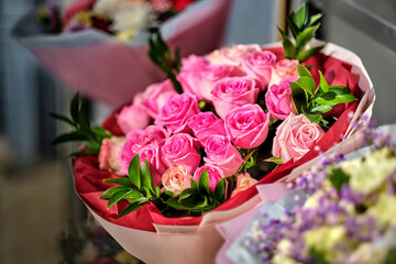 A bouquet of pink and white roses in red wrapping, with green leaves, against a background of other flowers.