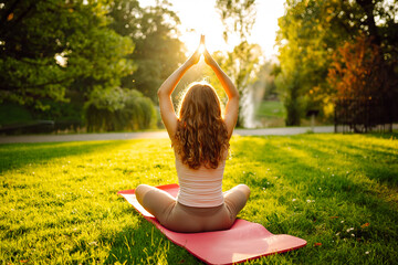 Morning yoga. Young beautiful woman  in sportswear stretching body on fitness mat at public park,...