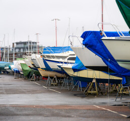 boats on stands with blue tarps in marina yard.
