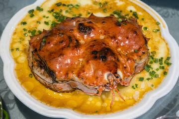 A white plate holds a steamed crab with its shell partially removed. The crab is on top of steamed egg and sprinkled with chopped scallions.