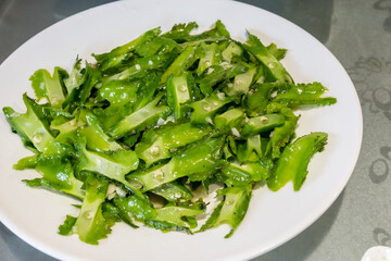 A white plate holds a serving of stir fried winged beans, with the green vegetable glistening . The beans are sliced and slightly charred, offering a delightful texture