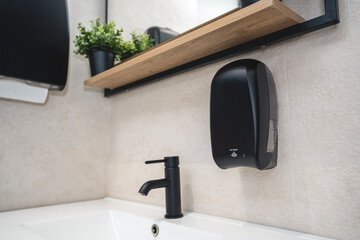  Black dispenser for electronic liquid soap anddispenser for paper towels in a modern bathroom.