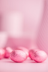 Chocolate easter eggs wrapped in pink colored foil on pink background.