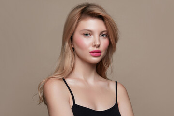 Fototapeta premium Beauty fashion portrait of a young blonde woman with a long hair, flawless clean skin, pink lips, and minimal makeup on a pastel beige background.