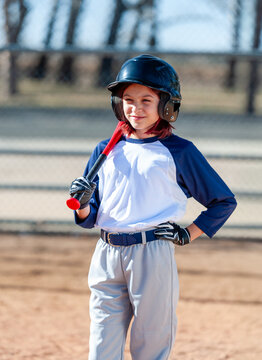 Young girl in little league baseball uniform with bat and helmet at home plate