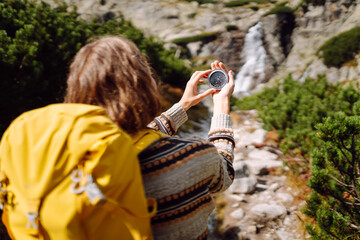 Compass in hand of woman tourist against the background of a mountain road. Choosing a path in...