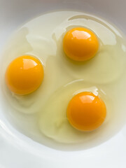 Three bright yellow raw chicken eggs in a white bowl.