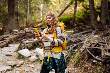 Smiling hiker using smartphone in forest.  Female tourist using mobile internet in woods. Blogging....