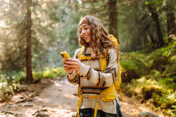 Smiling hiker using smartphone in forest.  Female tourist using mobile internet in woods. Blogging. Using smartphone gps