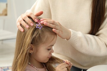 Fototapeta premium Mom putting cute accessories onto her daughter's hair at home, closeup