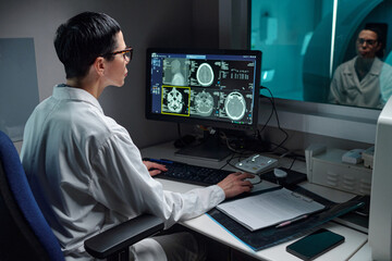 Radiologist analyzing detailed brain scans on computer monitor in modern medical lab. Person seen...