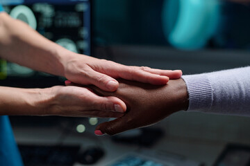 Naklejka premium Close-up of two people holding hands in a medical setting, one wearing a white sleeve and the other a professional uniform showing compassion and support