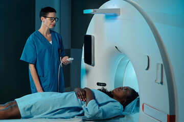 Medical professional wearing blue scrub assisting patient lying inside MRI scanner in clinical...