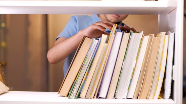 Boy eagerly reaching for a colorful book on a shelf, showing curiosity and thirst for knowledge in a library or at home