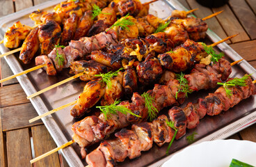 Closeup of appetizing grilled chicken and pork skewers garnished with fresh greens served on metal tray