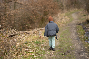 A girl with her back to the camera wearing a brown hat and jacket outside on a path in the woods....