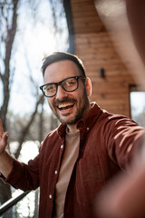 Happy entrepreneur waving hand while taking selfie on balcony