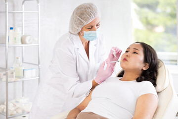Professional cosmetologist injecting the medication under patient skin in procedure cabinet