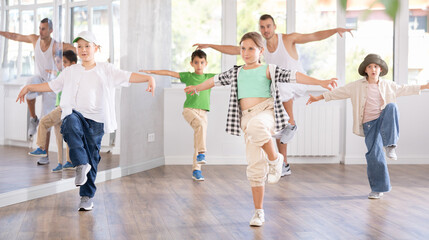 Obraz premium Emotional tween girl dancer rehearsing modern krump dance moves during group workout in kids studio under guidance of male instructor