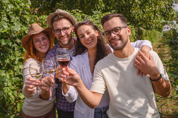 Group of happy friends enjoying a wine tasting at a vineyard, toasting with white wine glasses. They share laughter and smiles while celebrating together in a beautiful outdoor setting surrounded by l