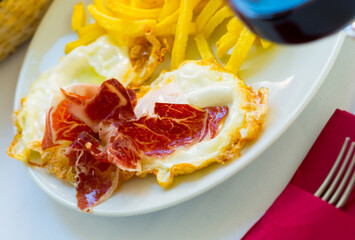 Traditional Spanish fried eggs with potatoes and ham served with glass of red wine..