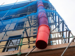 Blue mesh net on scaffolding and red plastic rubbish chute. Old building repair work. Construction...