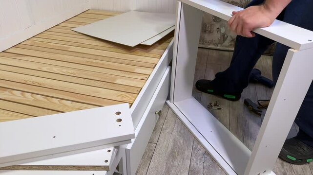 The man is assembling pull-out shelves for the sofa bed. He installs the bottom of the shelf.