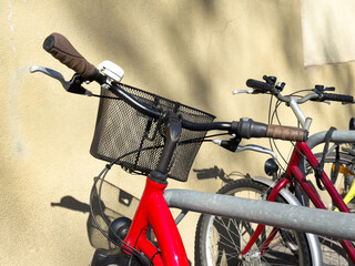 Red bicycle with basket parked at metal rack in urban setting