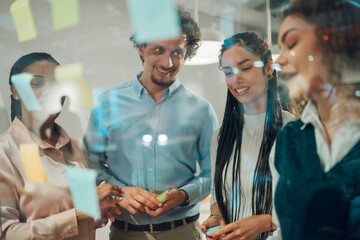 Businesspeople planning strategy using sticky notes on glass wall in office
